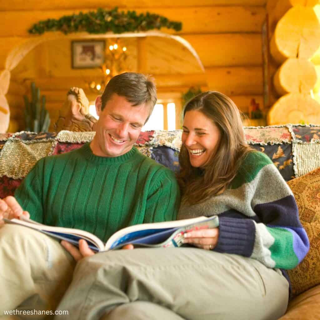 a couple sitting on a couch looking at a book together smiling