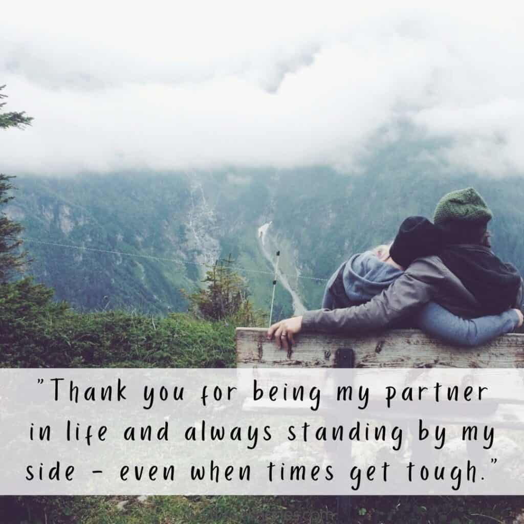 By my side appreciation quote at the bottom of a photo of a couple cuddling on a bench looking out at a mountain landscape.