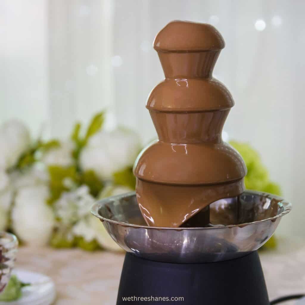 Chocolate fountain with blurred background of white flowers