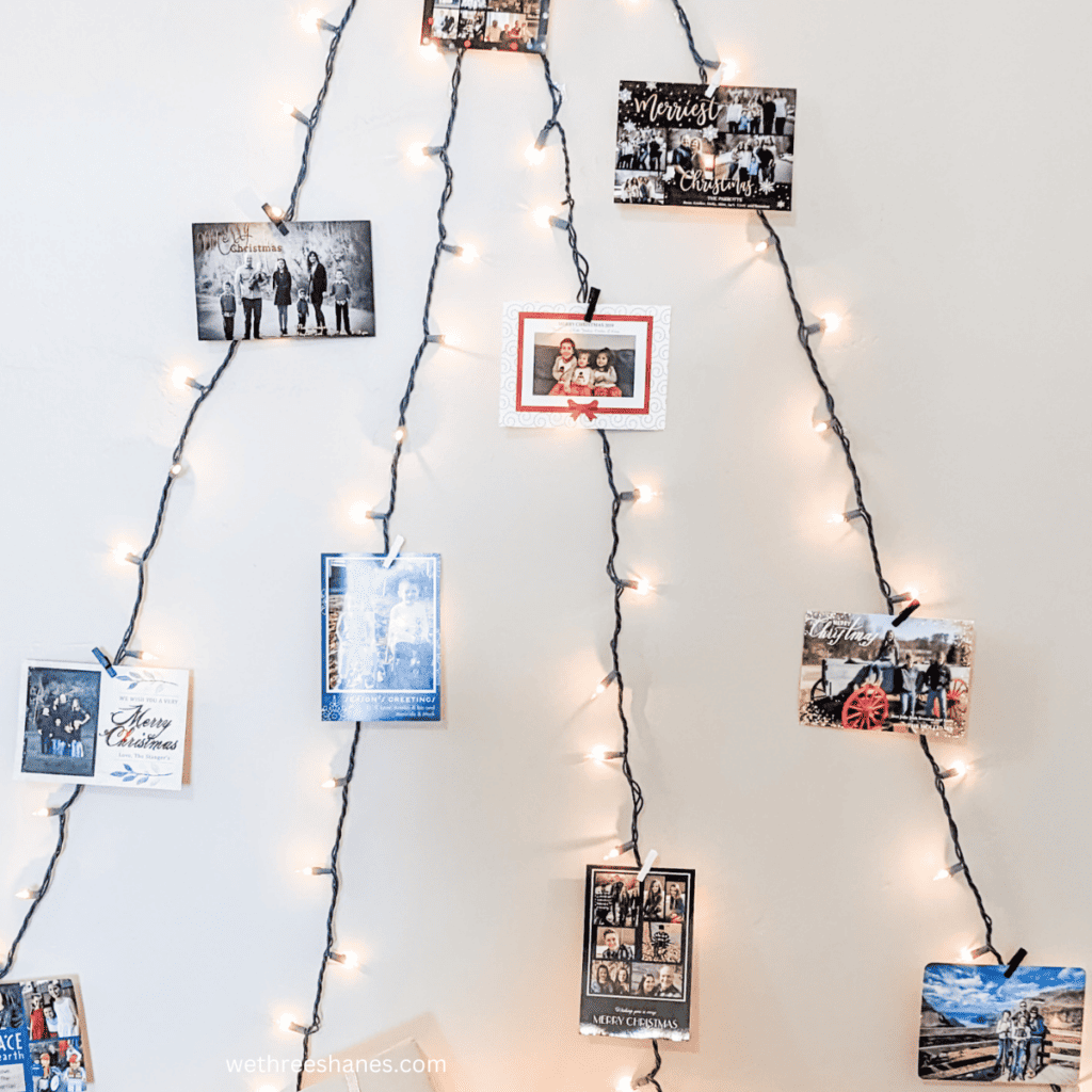 String lights in the form of a Christmas tree on the wall with Christmas cards clipped to the lights.