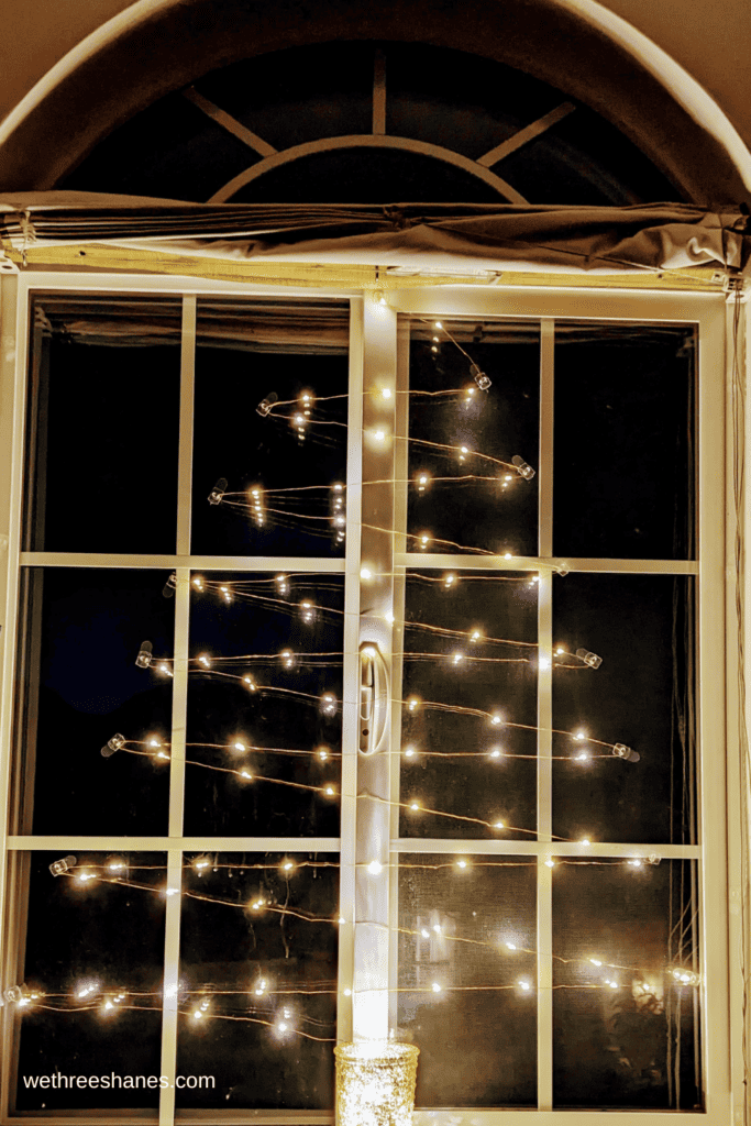 Fairy lights zig zag in a Christmas Tree pattern in a window.