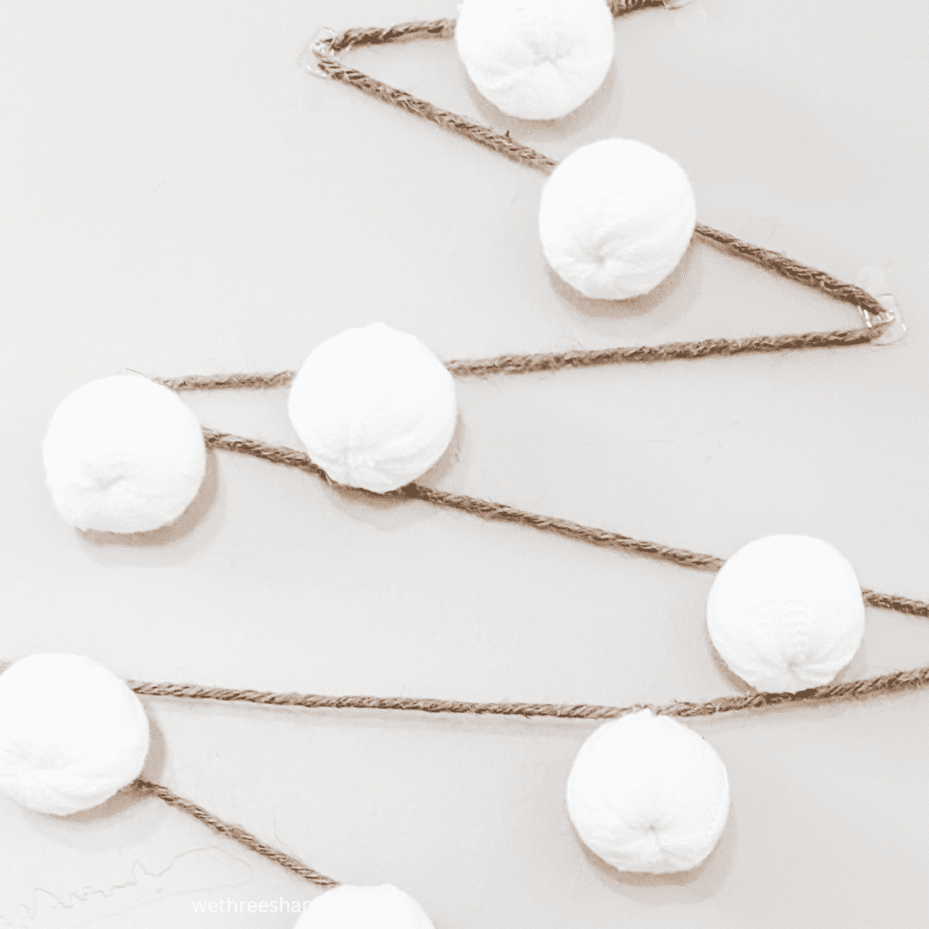 Thick twine and white ornaments in a zig zag pattern for a wall Christmas tree