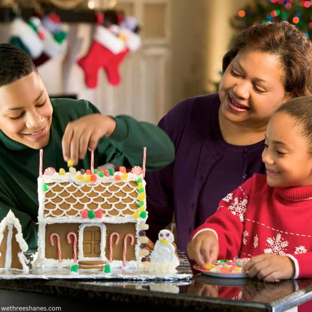 Mom and son and daughter building a gingerbread house together.