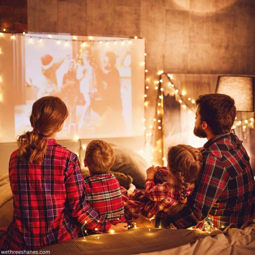 Family wearing matching plaid Christmas pajamas while watching a Christmas movie on a big screen.