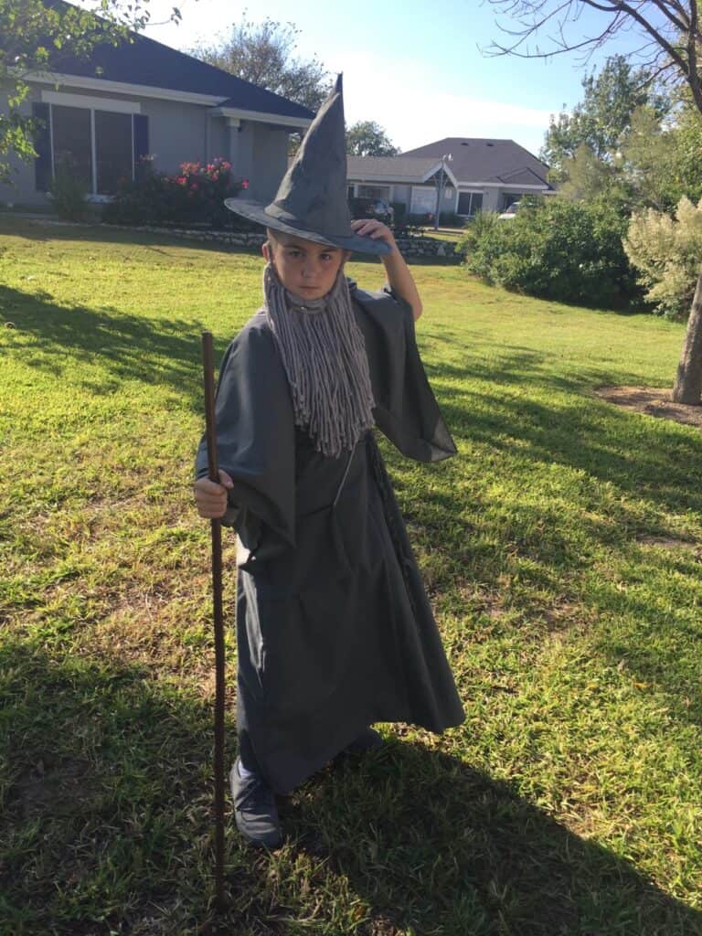 Young boy dressed in grey robes with a grey beard, pointy hat, and staff.