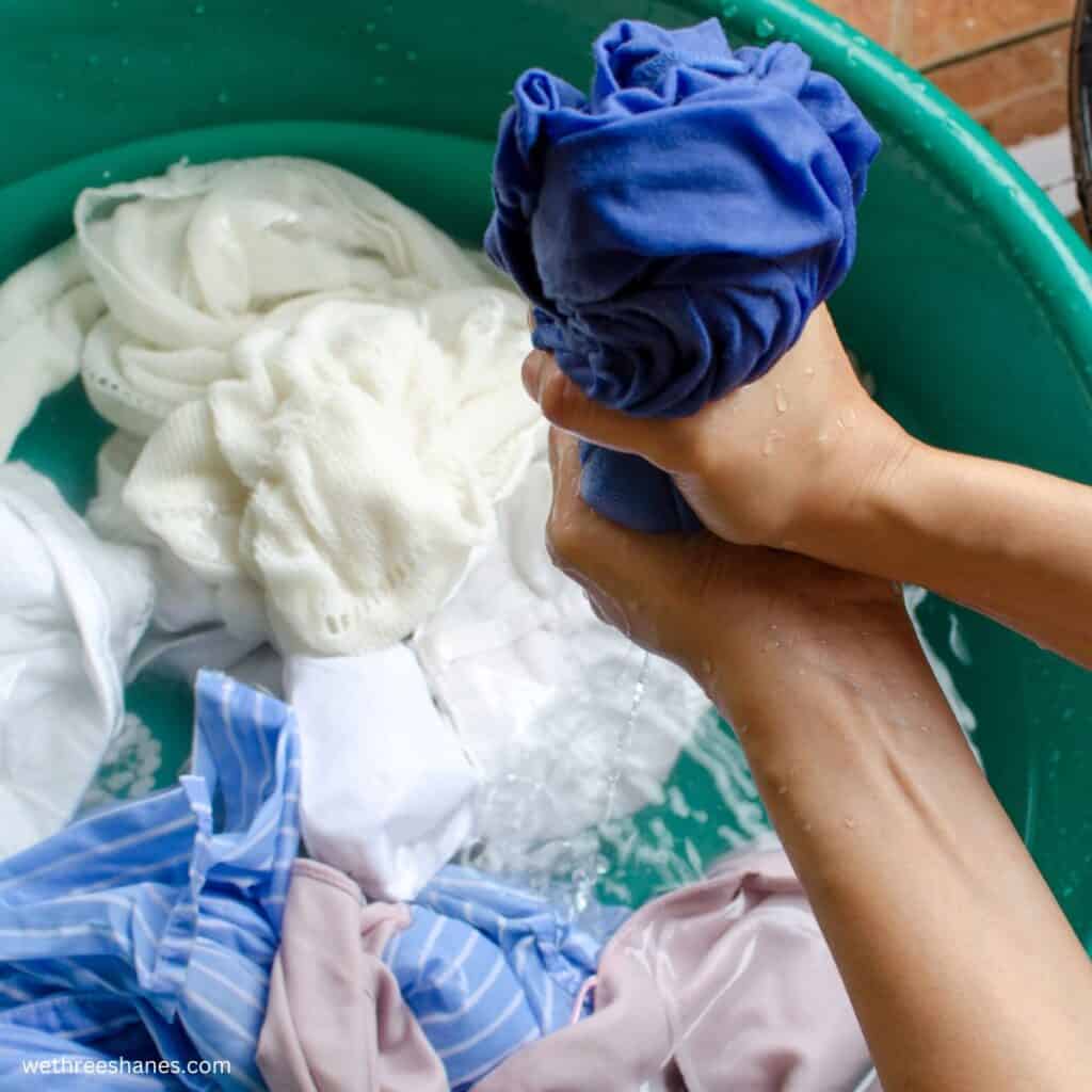 soaking clothes in a bucket of water and someone is ringing out the water of one of the clothing items.