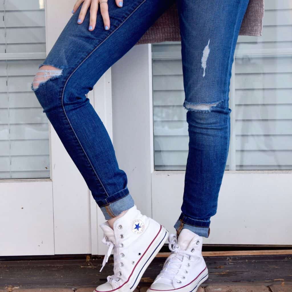 Someone wearing ripped jeans and white, high-top converse