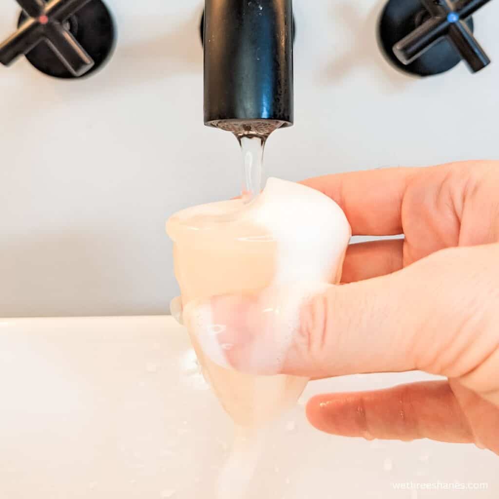 Someone holding a soapy menstrual cup under water to rinse it off.