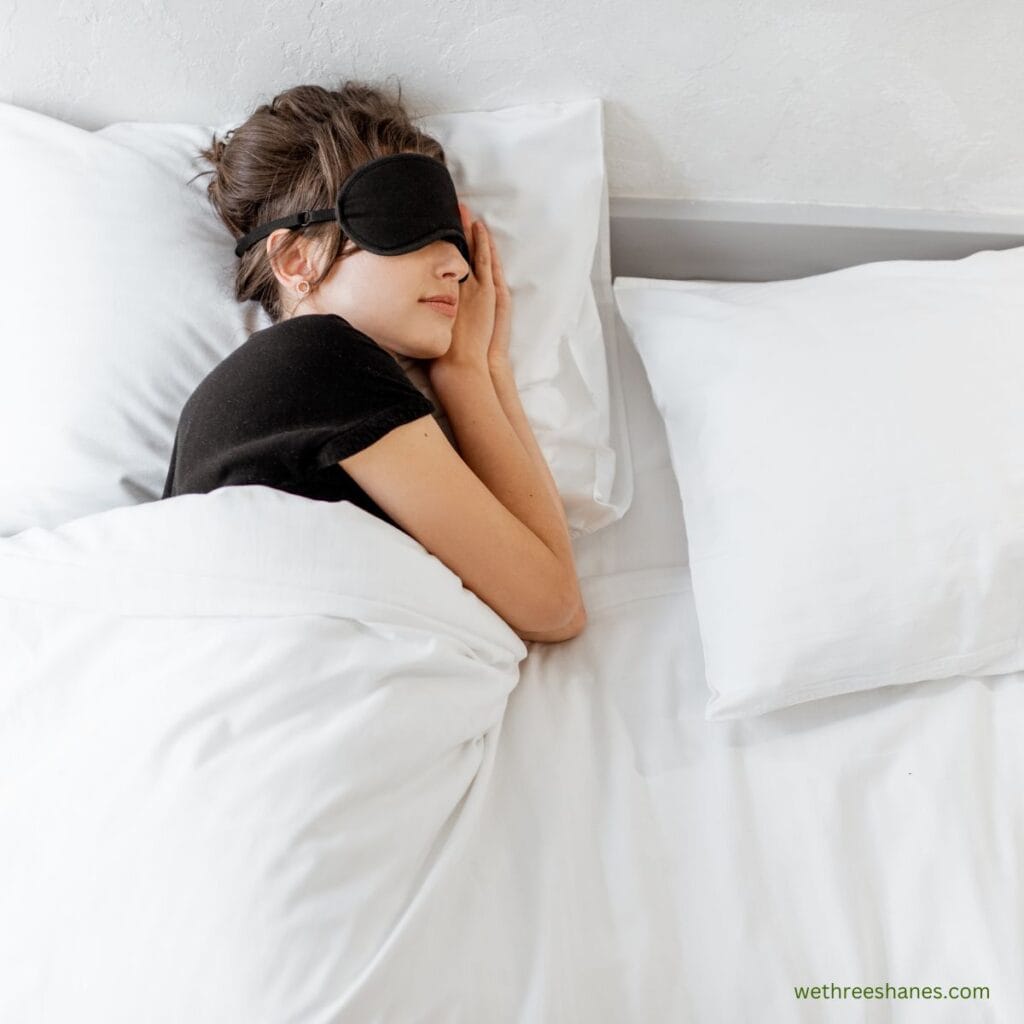 picture of a woman sleeping with an eye mask on in a bed with all white bedding. She is practicing self-care