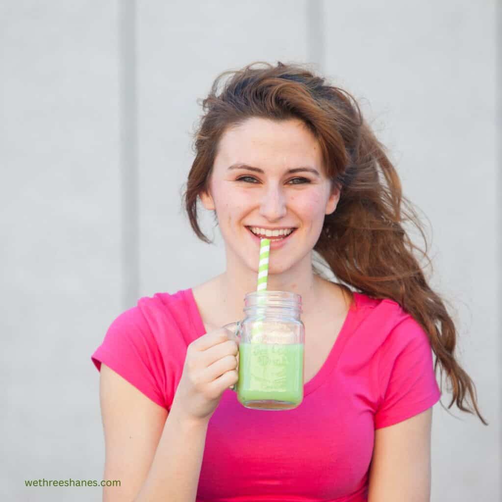 Picture of a smiling teenage girl drinking a smoothie out of a glass mason jar cup with a straw.  